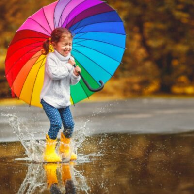A young girl with a colourful umbrella jumping in puddles
