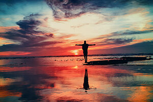 Man standing on rocks with arms outstretched looking at sunrise
