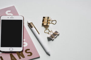 phone with pen, book and clips on white surface