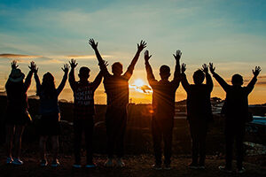 Row of young people with arms in the air in front of a sunset
