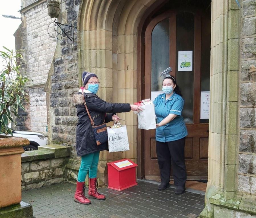Anna Chaplain hands over a gift bag of knitted crosses to a member of staff outside a care home.