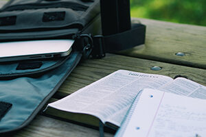 Open Bible with laptop bag and notebook on an outdoor table