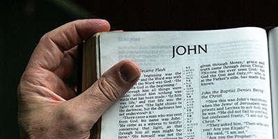 Hand holding open a Bible at the gospel of John