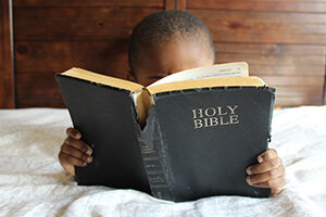 Boy reading Bible while lying on bed