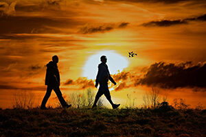 Silhouettes of two people walking in front of sunset