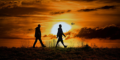 Silhouettes of two people walking in front of sunset