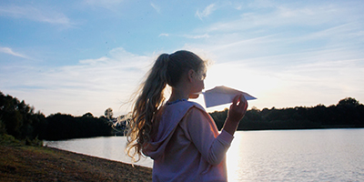Girl holding a paper plane standing by a lake