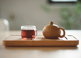 A small pot and clear glass of tea together on a wooden tray