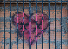 Black and pink graffiti of a heart shape on a brick wall behind bars