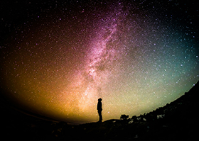 Silhouette of a man looking up at a night sky full of stars